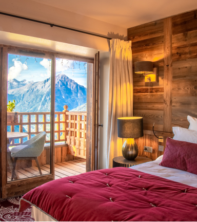 Chambre avec balcon vue sur les montagnes. Mur en bois et couvre lit rouge velours.